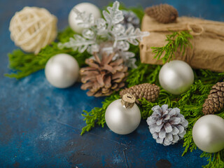 Fototapeta na wymiar Stylish composition of fir branches, cones, white Christmas balls and an original wrapped gift on a blue background. New Year, Christmas, postcard, invitation, banner, poster.