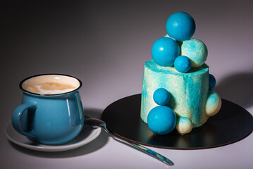 Obraz na płótnie Canvas Blue birthday cake with balls of white and blue chocolate with a cup of blue coffee, on a gray background. Shadow and light, contrast