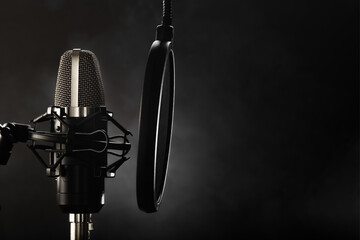 Professional studio microphone and pop filter. Dark gray background. Minimalism. Recording studio, vocals, conversational genre, radio broadcasting, music, clear sound.