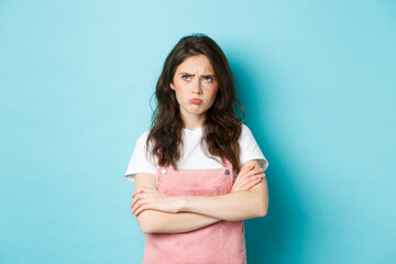 Disappointed sad brunette girl pouting, cross arms on chest and looking at upper left corner unfair...