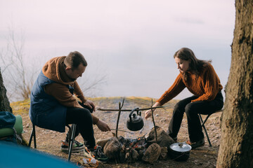 A married couple fries marshmallows on the shore of the lake with a tent. Hiking camp with a bonfire in the forest.