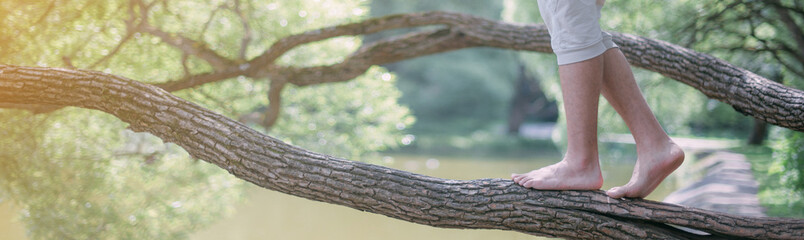 Obraz premium A man walks barefoot on a large tree branch. Close-up of the legs.