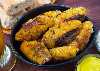 Dish of tasty fried chicken wings served in black bowl, two sauses on table