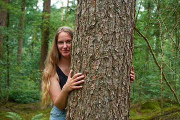 A portrait of a young Italian woman behind a tree in a forest