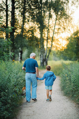 Obraz premium Grandfather walks with his grandson and dog in the park