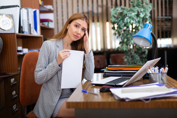 Portrait of a thoughtful young businesswoman sitting at her workplace in front of a computer with important document in the ..office