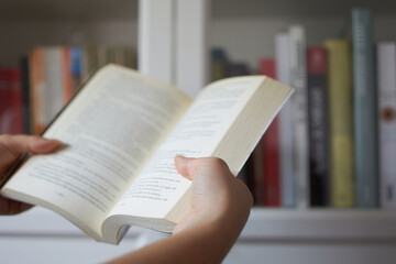 Hands of woman reading a book next to a bookcase