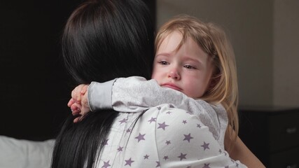 Mom soothes her daughter, child cries in room in arms of his mother. Loving young mother hugs and...