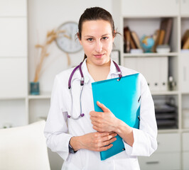 Young female doctor stands with a folder of documents in the office at the clinic
