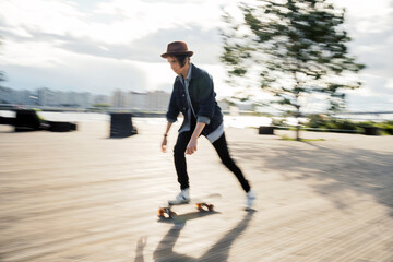 A blurry photo in motion. A young hipster man and his hobbies. A freelancer in a hat rides a skateboard in the city.