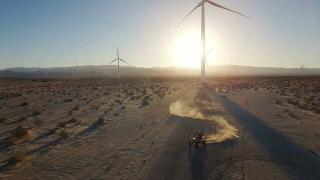 4k Aerial of ATV riding through dust cloud donuts with wind turbine