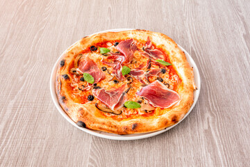 Small pizza with serrano ham, black olives, basil leaves, slices of mushroom and mozzarella cheese