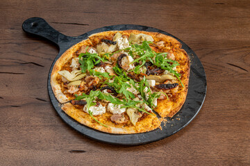 Small thin crust pizza with buffalo cheese, artichoke hearts, arugula and pork torozos on a black tray