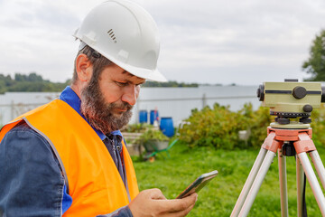 A civil engineer with an optical level looks into a mobile phone.