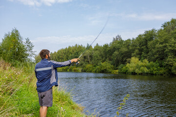 A man with a beard is fishing on the river, casting a line.