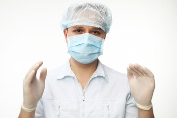 A young male doctor wearing mask stands with gloved hands, preparing for a patient examination or surgery