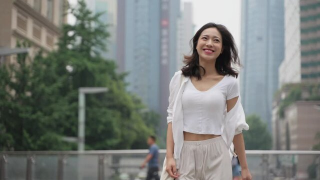 happy young asian woman walking in the urban city street wear white shirt at summer day in Chengdu China