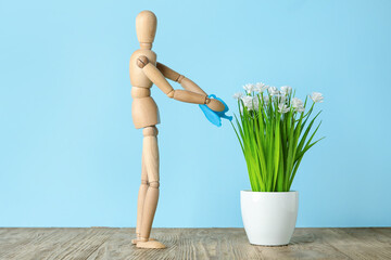 Wooden mannequin watering plant on color background. Concept of gardening