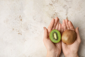 Female hands with fresh kiwi fruit on grunge background