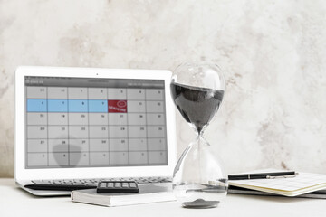 Hourglass and laptop with calendar on light table. Deadline concept