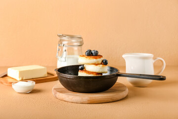 Frying pan with tasty cottage cheese pancakes and blueberry on color background