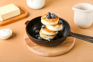 Frying pan with tasty cottage cheese pancakes and blueberry on color background