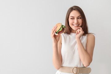 Beautiful young woman with tasty vegan burger on light background