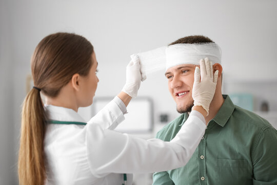 Doctor applying bandage onto head of young man in clinic