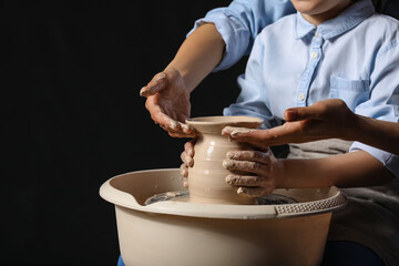 Little girl with her mother making ceramic pot on dark background, closeup
