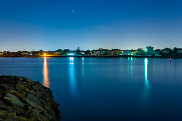 Obraz premium Long exposure of coastal town at night with lights reflecting in the blurry water