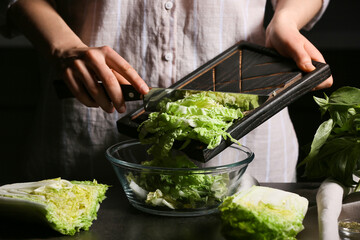 Woman cutting fresh chinese cabbage on table, closeup