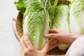 Woman with fresh chinese cabbage on light background, closeup