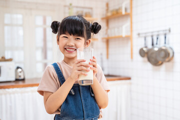 Portrait of Asian little kid holding a cup of milk in kitchen in house