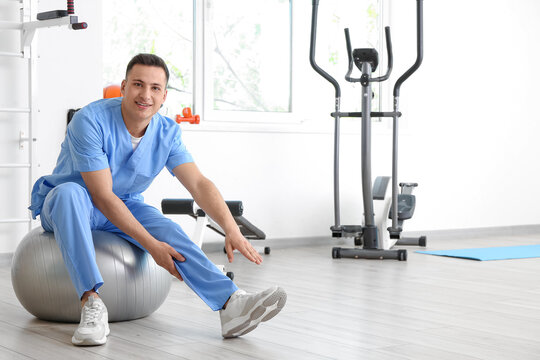 Male physiotherapist demonstrating exercise with fitball in rehabilitation center