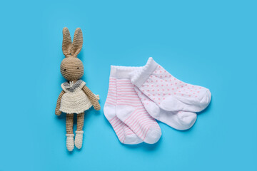 Baby socks and toy on color background