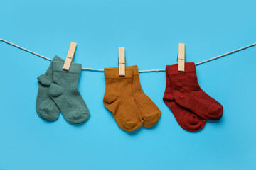 Different baby socks hanging on rope against color background