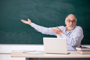 Old male teacher in front of green board