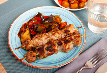 Traditional georgian dish shish kebab or shashlik, grilled pork meat served with braised eggplants, pepper and tomatoes
