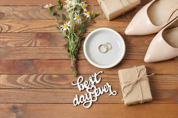 Fototapeta na wymiar Tray with wedding rings, bride accessories and text BEST DAY EVER on wooden background