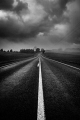 A lonely country road shrouded in mysterious moody clouds and mist in black and white