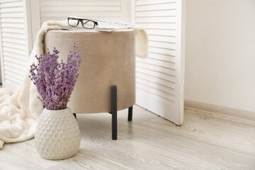 Vase with beautiful lavender flowers and stylish pouf in room