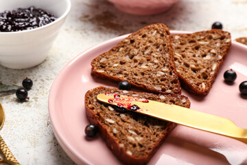 Wholegrain bread in plate and delicious black currant jam on light table, closeup