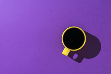 A yellow cup of coffee on a bright purple background.