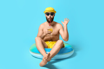 Young man with inflatable ring drinking cocktail on color background