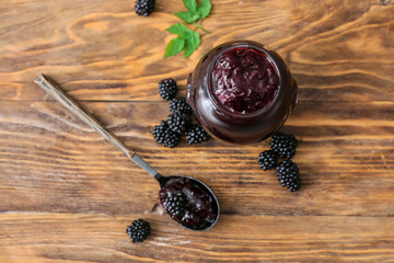 Jar and spoon with tasty blackberry jam on wooden background