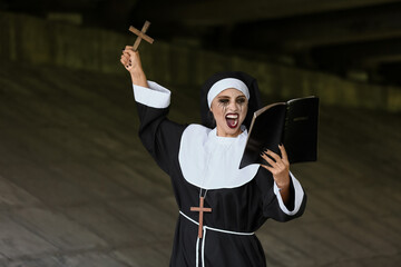 Woman dressed for Halloween as nun with cross and Bible on dark background