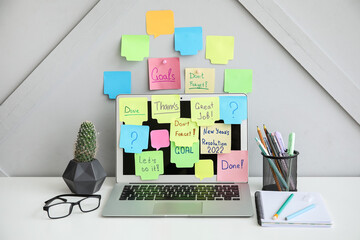 Modern workplace with laptop and sticky notes near light wall