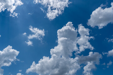 White cotton like puffy cumulus clouds against a blue sky with the suns rays shining.