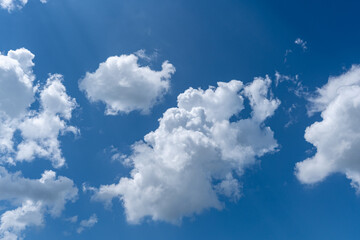 White cotton like puffy cumulus clouds against a blue sky with the suns rays shining.