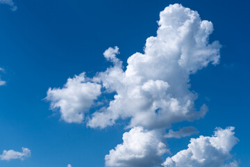 White cotton like puffy cumulus clouds against a blue sky with the suns rays shining.